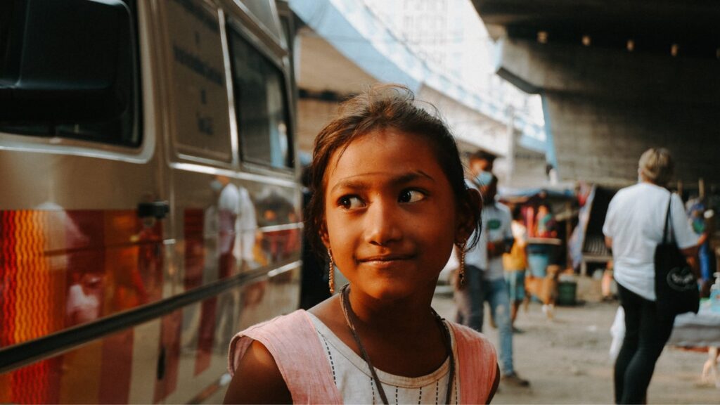 Young girl smiling on a busy street, filmed for the Hope Foundation