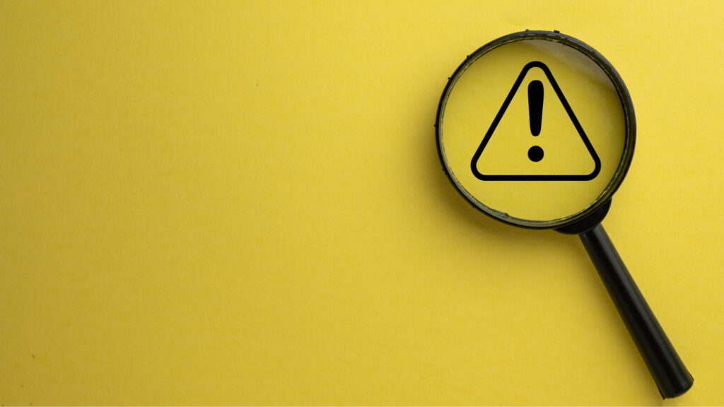 Magnifying glass over a warning symbol on a yellow background