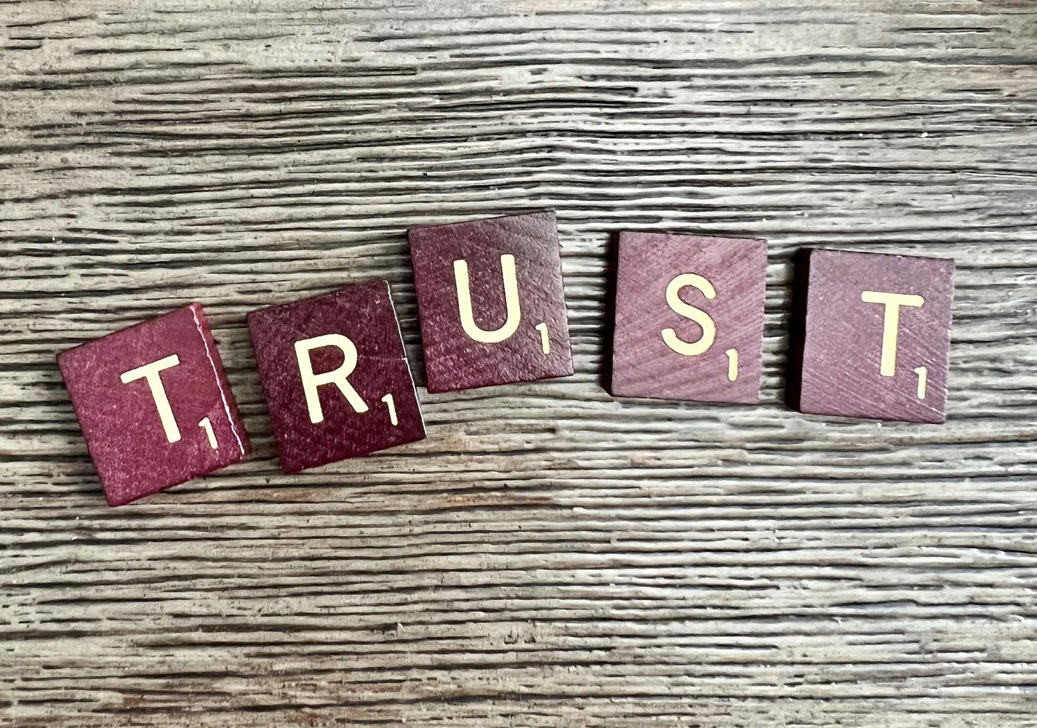 Scrabble tiles spelling 'Trust' on a wooden surface