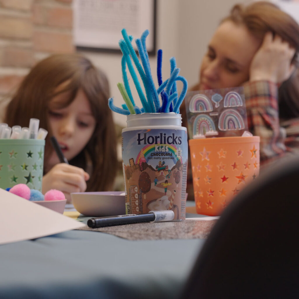 Child drawing at a craft table next to a Horlicks jar full of pens