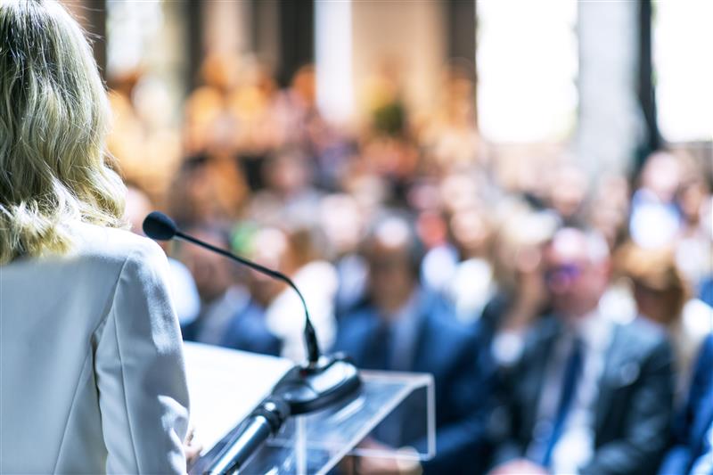 Politician speaking at a podium to a seated conference audience
