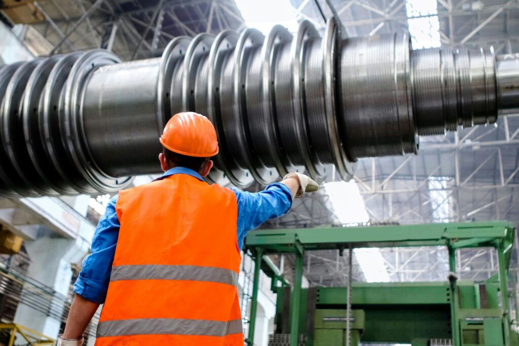 Engineer in a hard hat and hi-vis vest inspecting large machinery in a factory