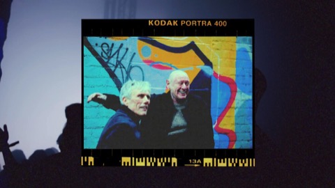 Film frame of two older men in front of a graffiti wall