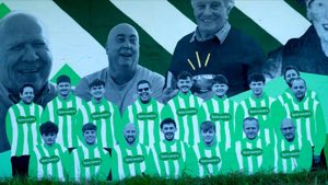 Two men in front of a wall of cut-out football players in green and white striped kits