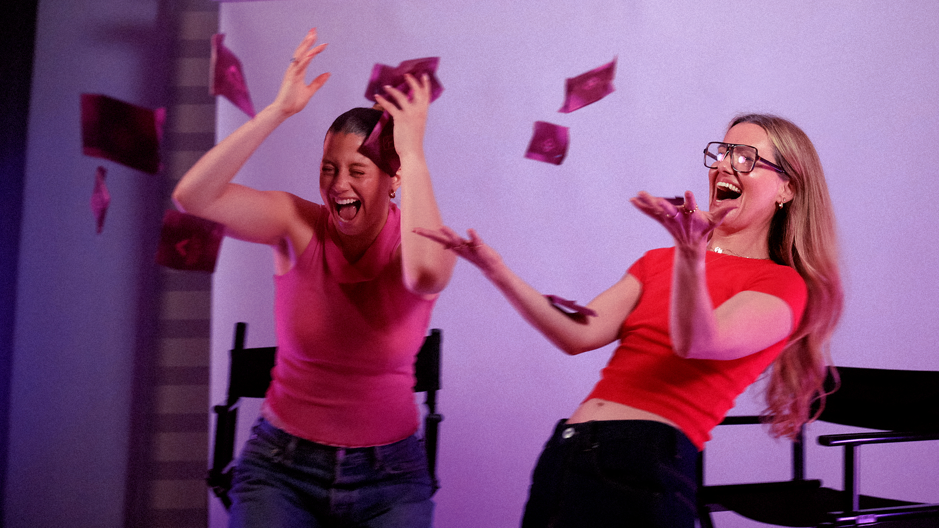 Two women laughing and throwing paper in the air during a studio shoot
