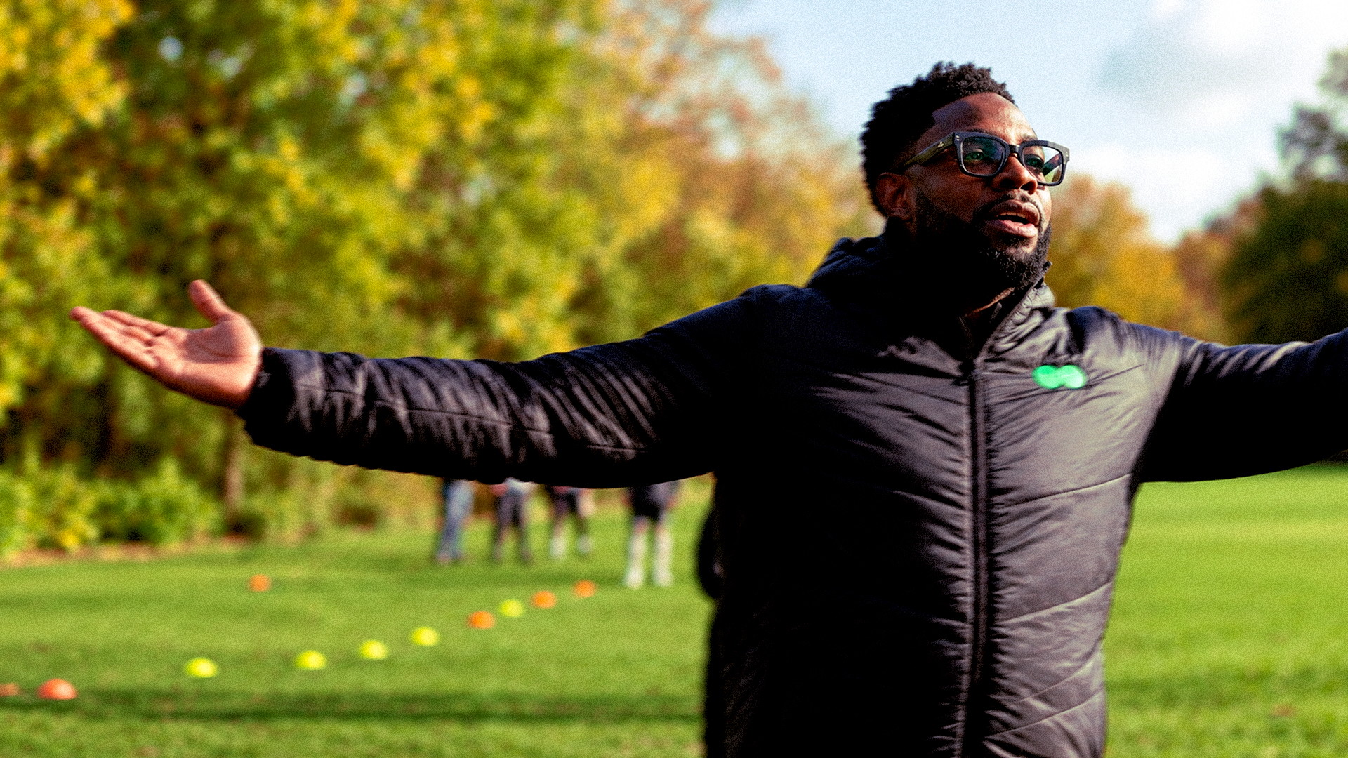 Man in sunglasses with arms outstretched on a playing field during a campaign shoot