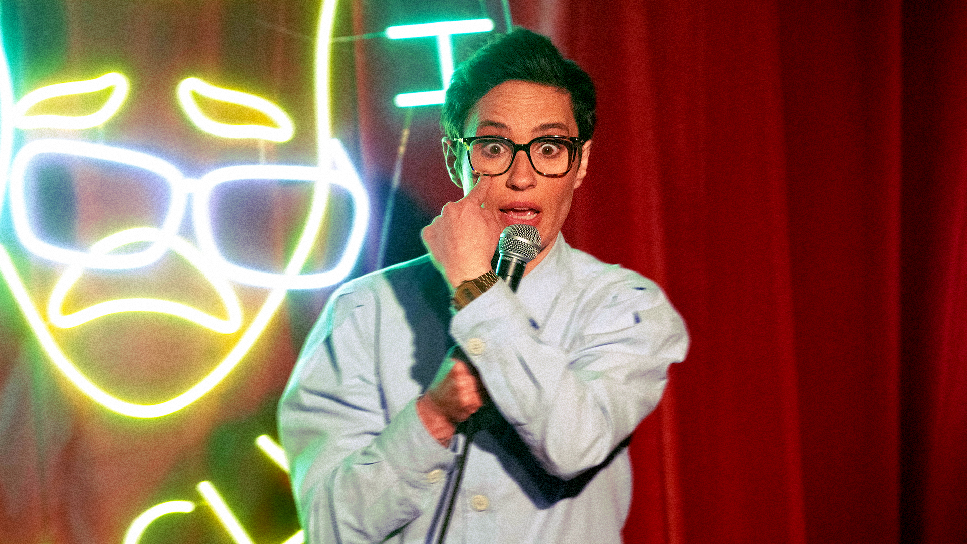 Speaker with a microphone on stage beside a neon sign