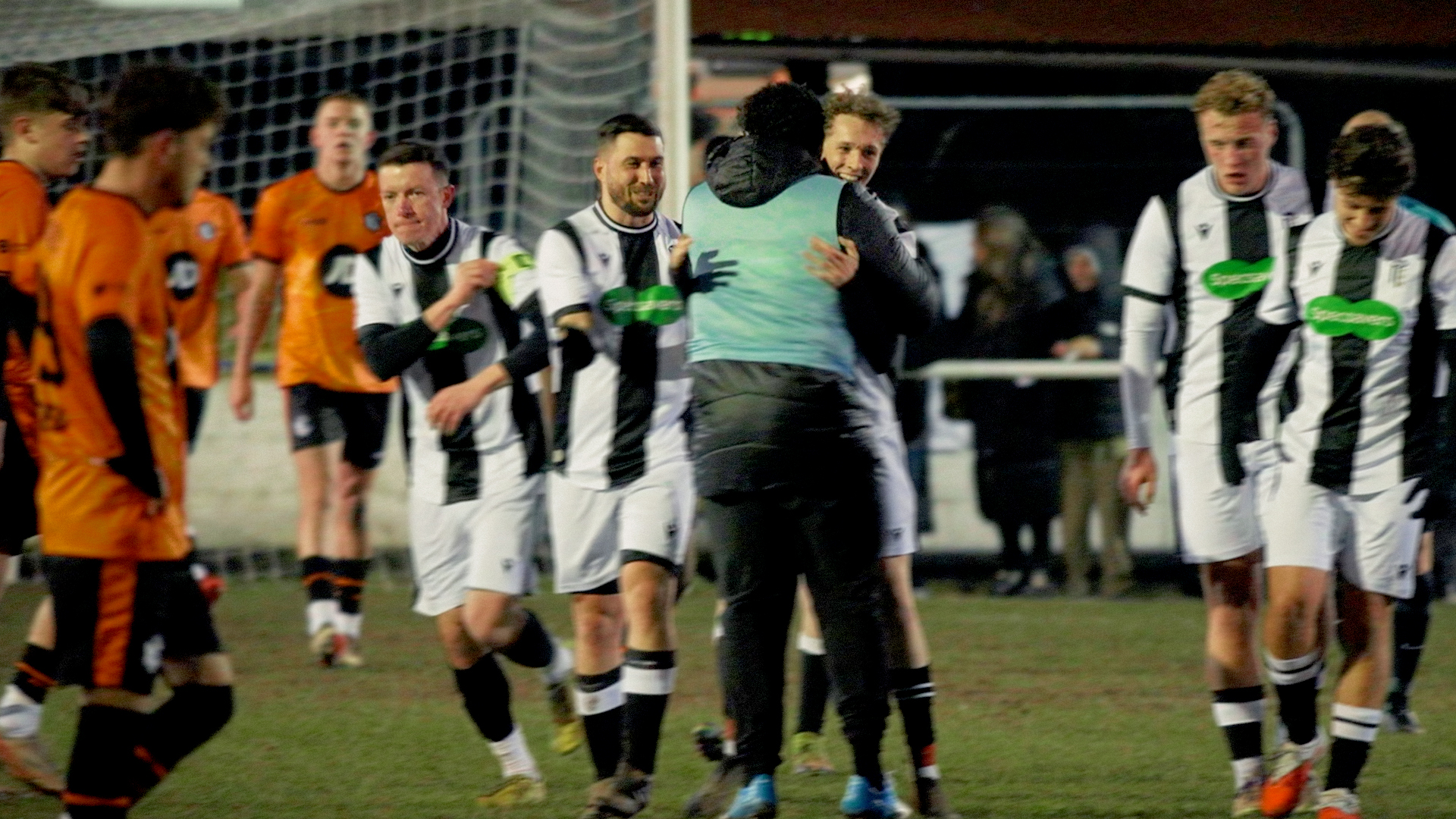 Grassroots footballers in black and white kits celebrating on the pitch