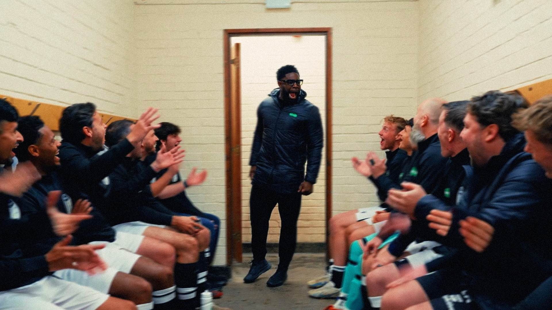 Coach walking into a changing room as seated players applaud