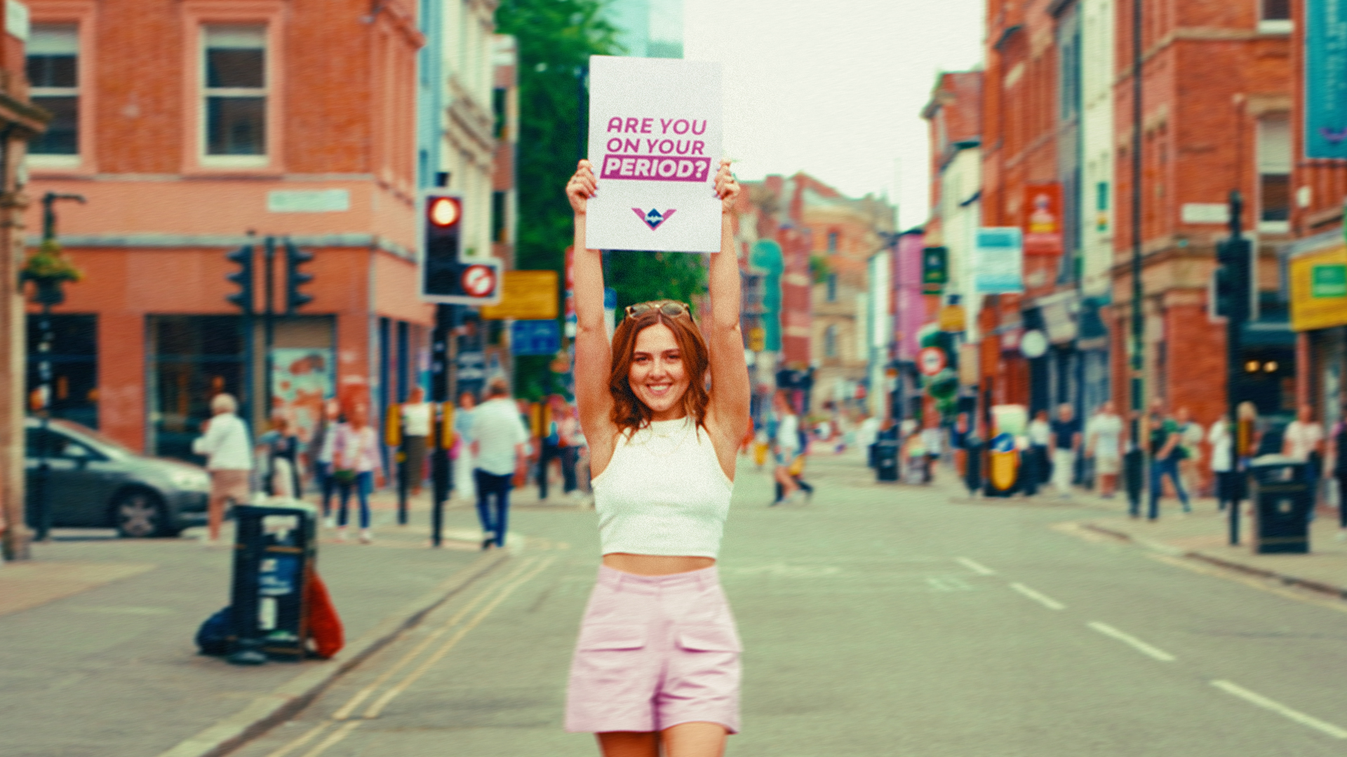 Woman holding a sign asking 'Are you on your period?' in the middle of a Manchester street