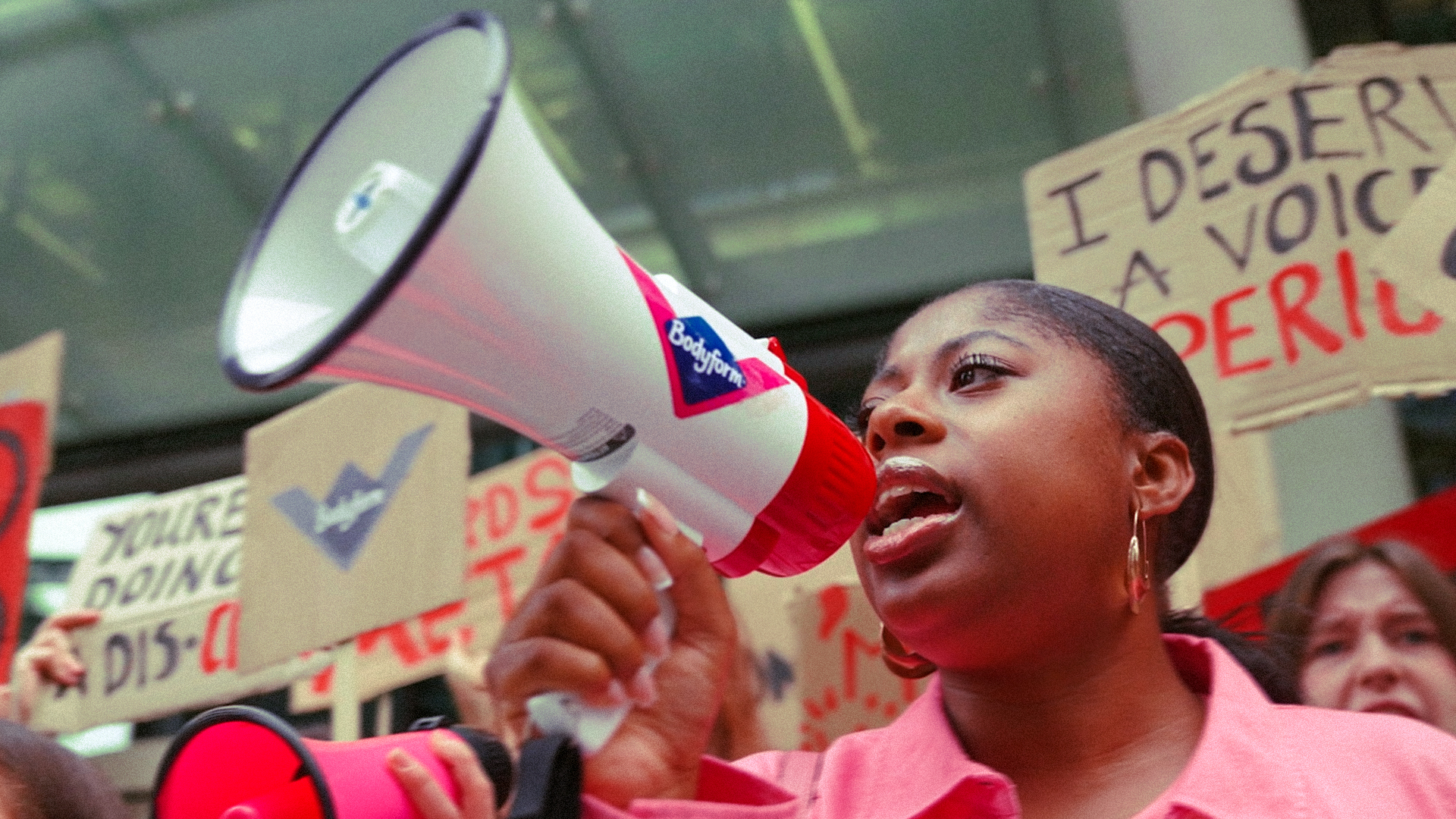 Woman shouting through a Bodyform megaphone at a protest with placards