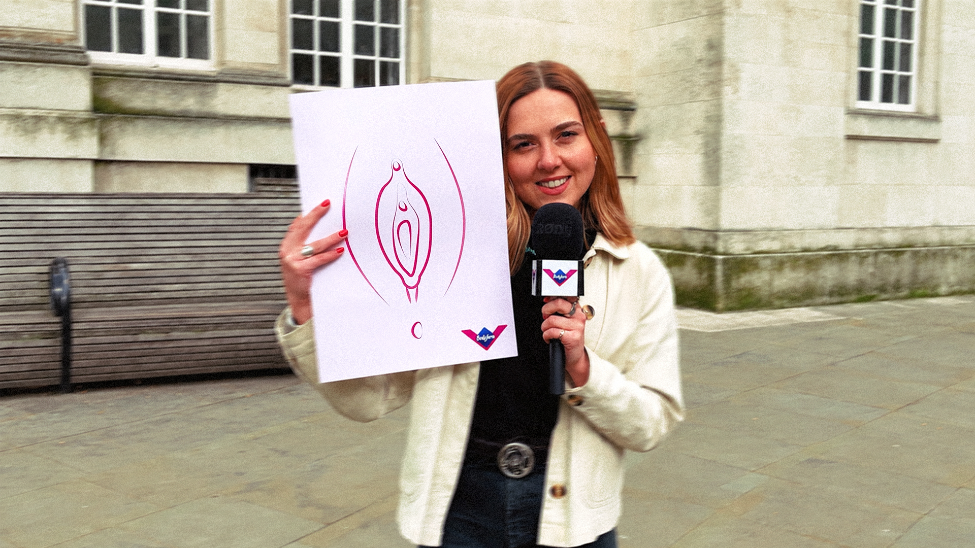 Presenter holding a vulva illustration and a branded microphone outside a Manchester building